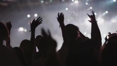 在音乐表演中，手举着手面对着黑色灯光舞台的人的背景轮廓